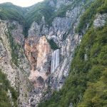 Waterfall cascading down a rocky canyon with lush greenery.